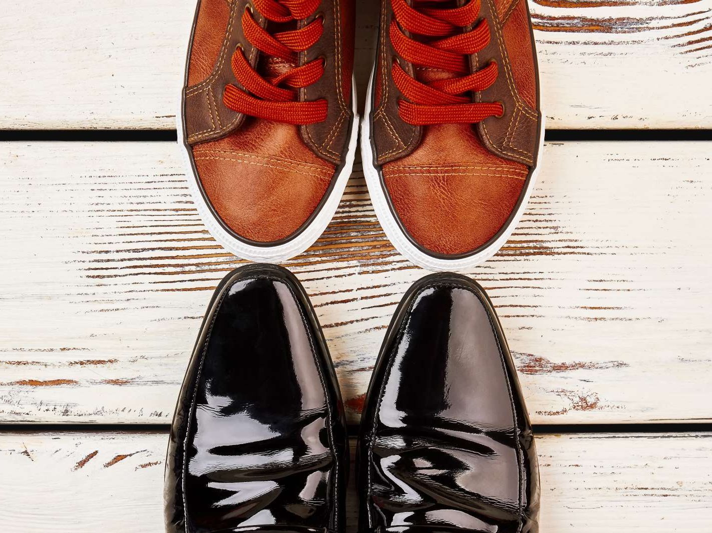 Zwei Paar Schuhe auf einem Holzboden, ein Paar Sportschuhe und ein Paar elegante Lederschuhe