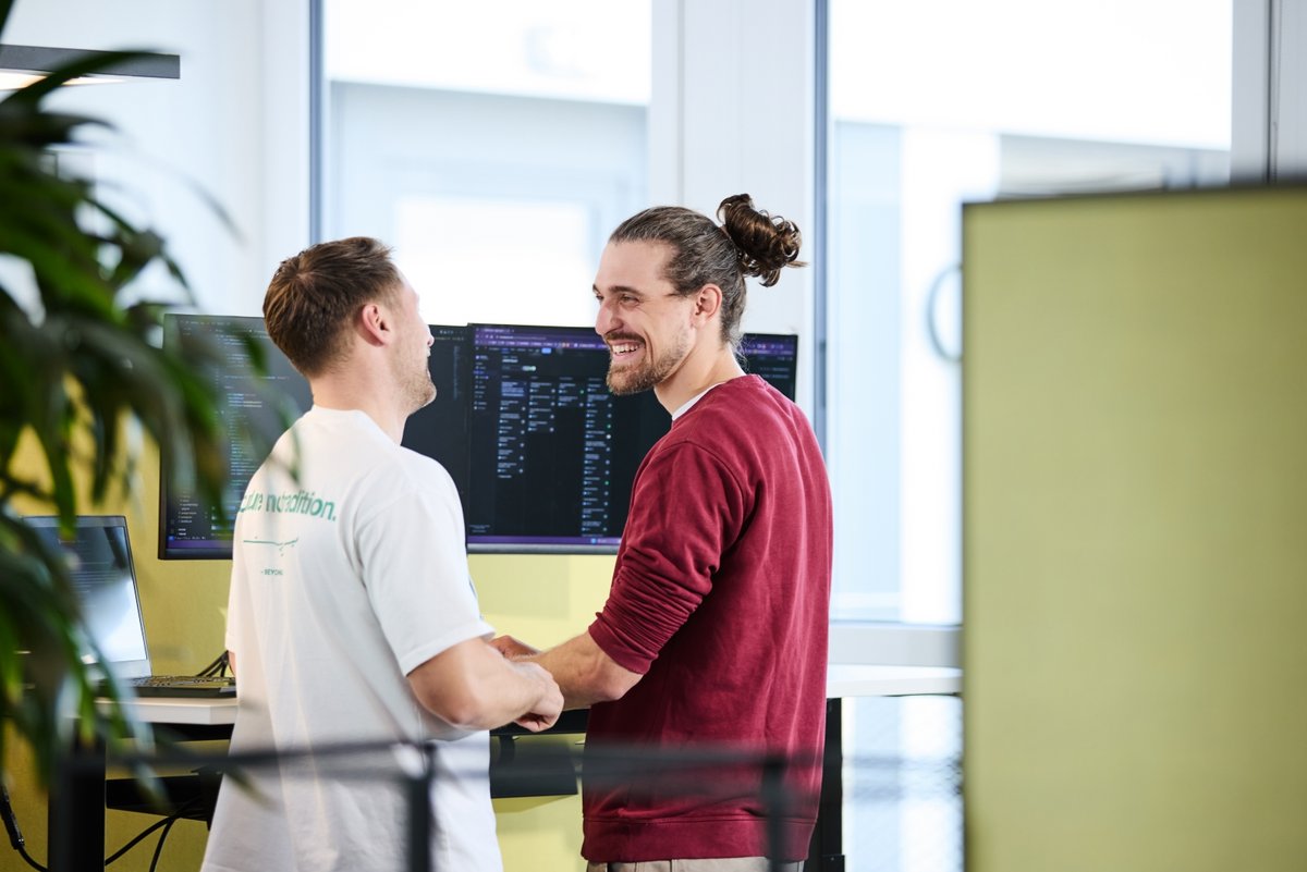 Zwei lise-Entwickler stehen vor einem Computer und schauen sich lachend an