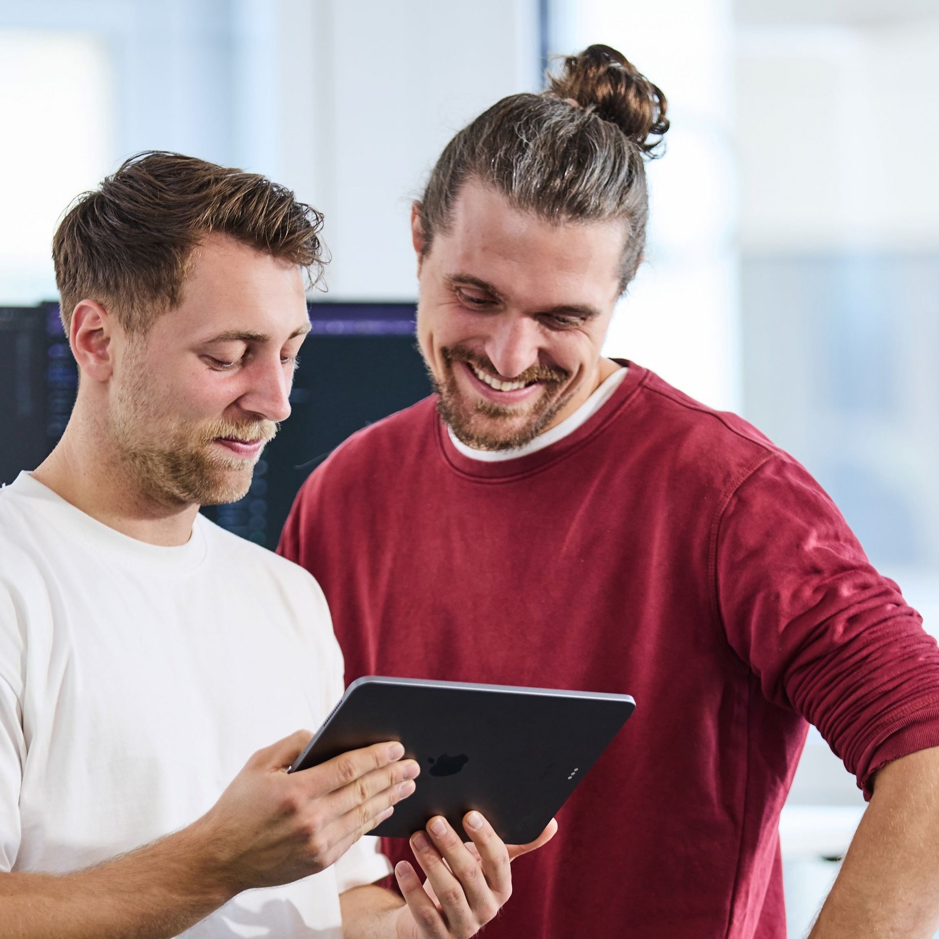 Ein lise-Entwickler zeigt einem anderen seine App-Entwicklung auf dem iPad, woraufhin der andere strahlt