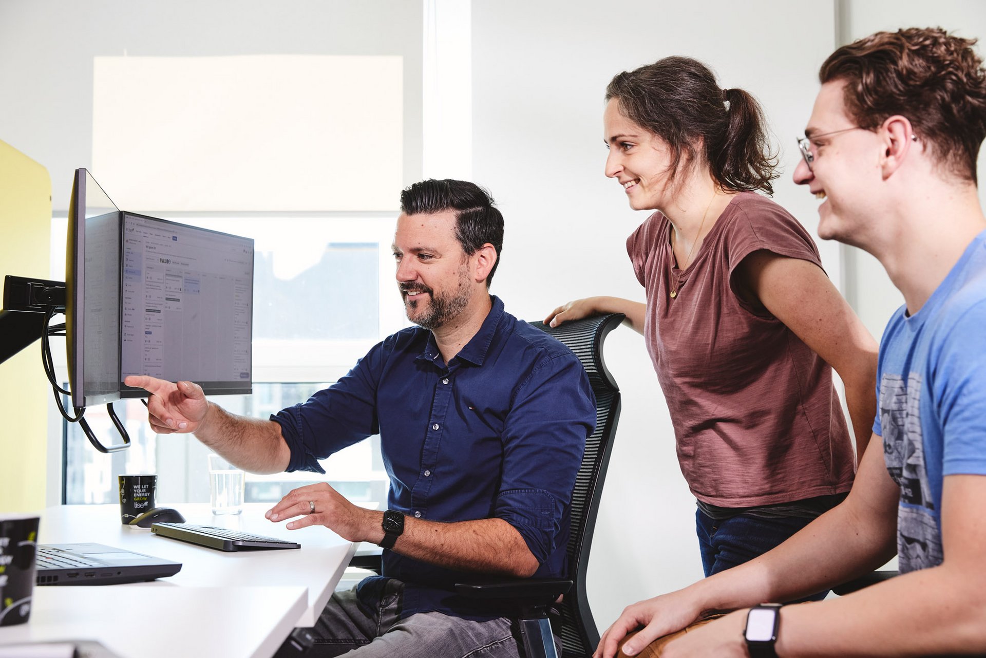 Dri lise Koleg:innen besprechen sich am Computer. Ein Kollege zeigt auf den Bildschirm.