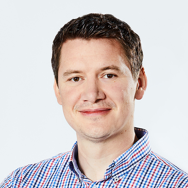 Ein lise-Unit Head in einem karierten Hemd und brauen Haaren lächelt in die Kamera