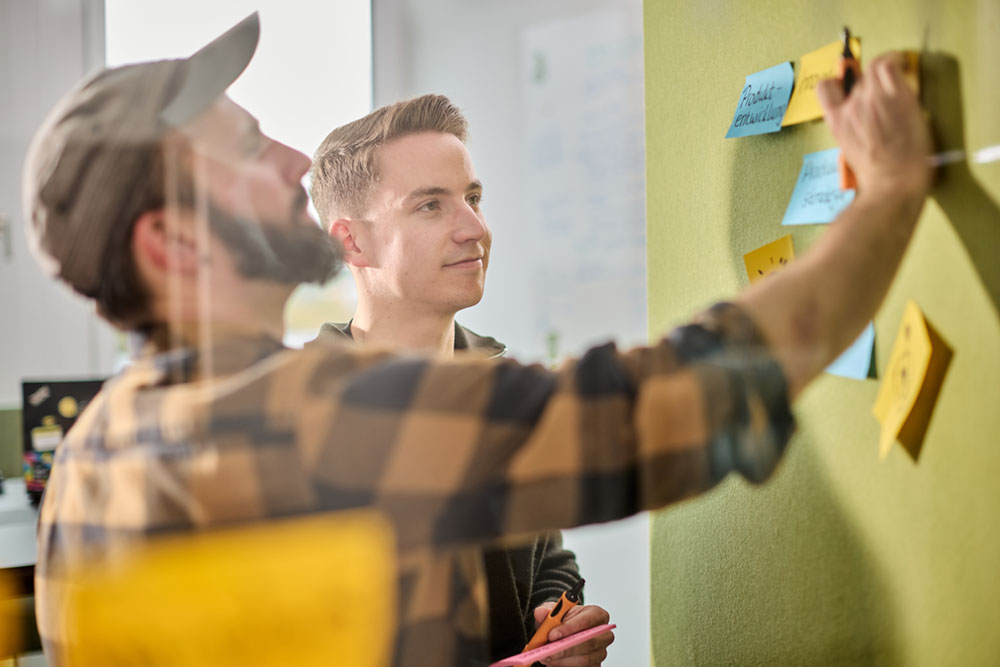 Zwei lise-Mitarbeiter sammeln zusammen Wünsche der User an einer Pinnwand